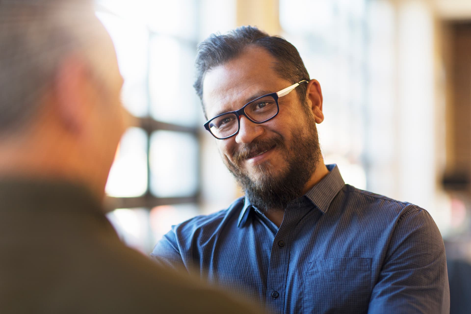 Male wearing glasses looks to another person in the foreground with a soft smile