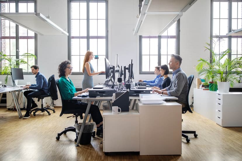 Office environment with a row of desks. Four workers are looking at their screens. 