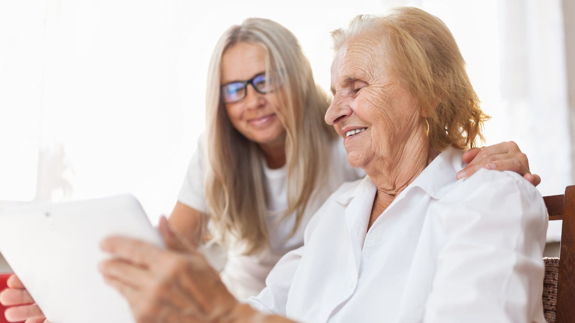 Two older adults seated together indoors reviewing information on a tablet, illustrating shared planning and guidance during an aged care assessment.