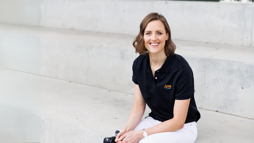 Ellie Cole in black polo top sitting on white stone steps
