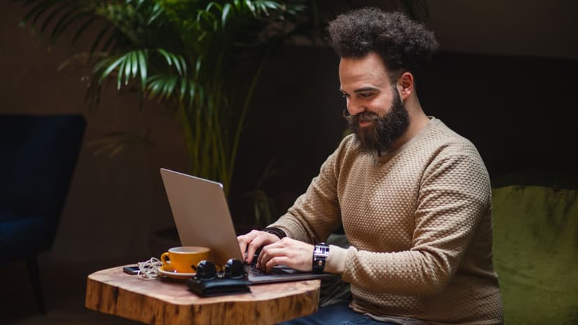 A man sits and smiles with a laptop