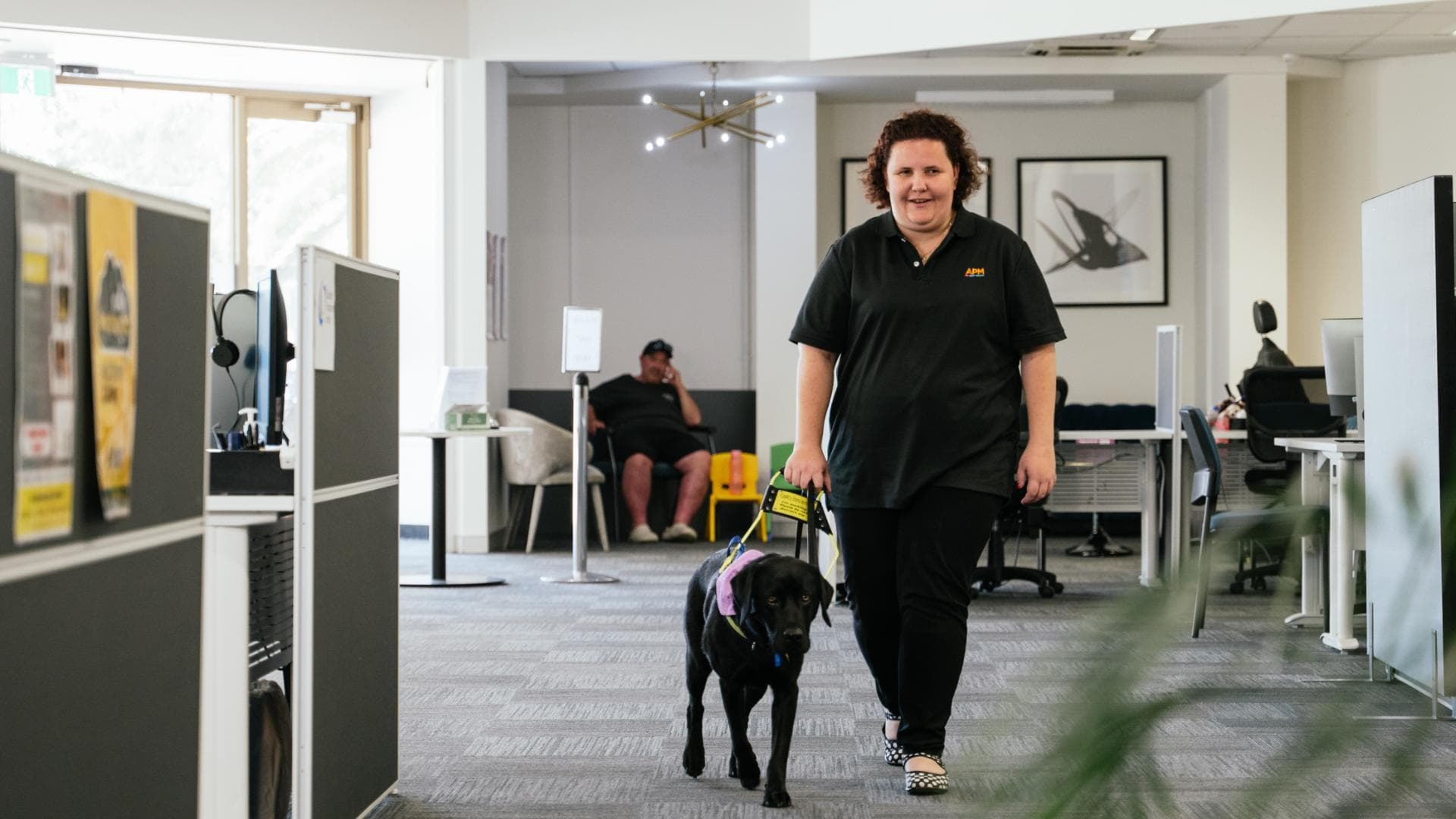 Ayesha walking in an APM office with her guide dog for the blind.