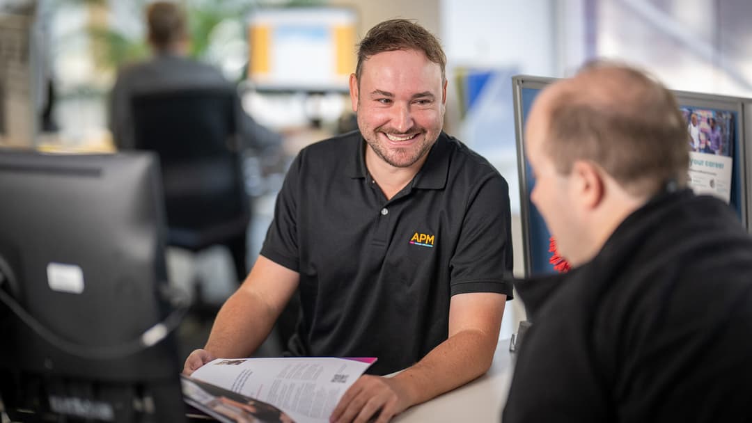 An APM employee in a black polo smiles in conversation with a DES participant