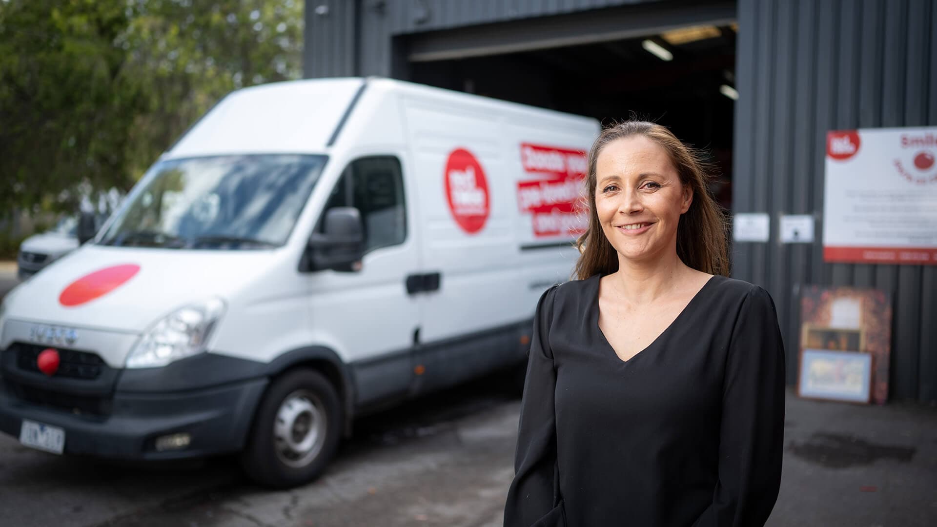 A woman in a black top smiles outside a business warehouse