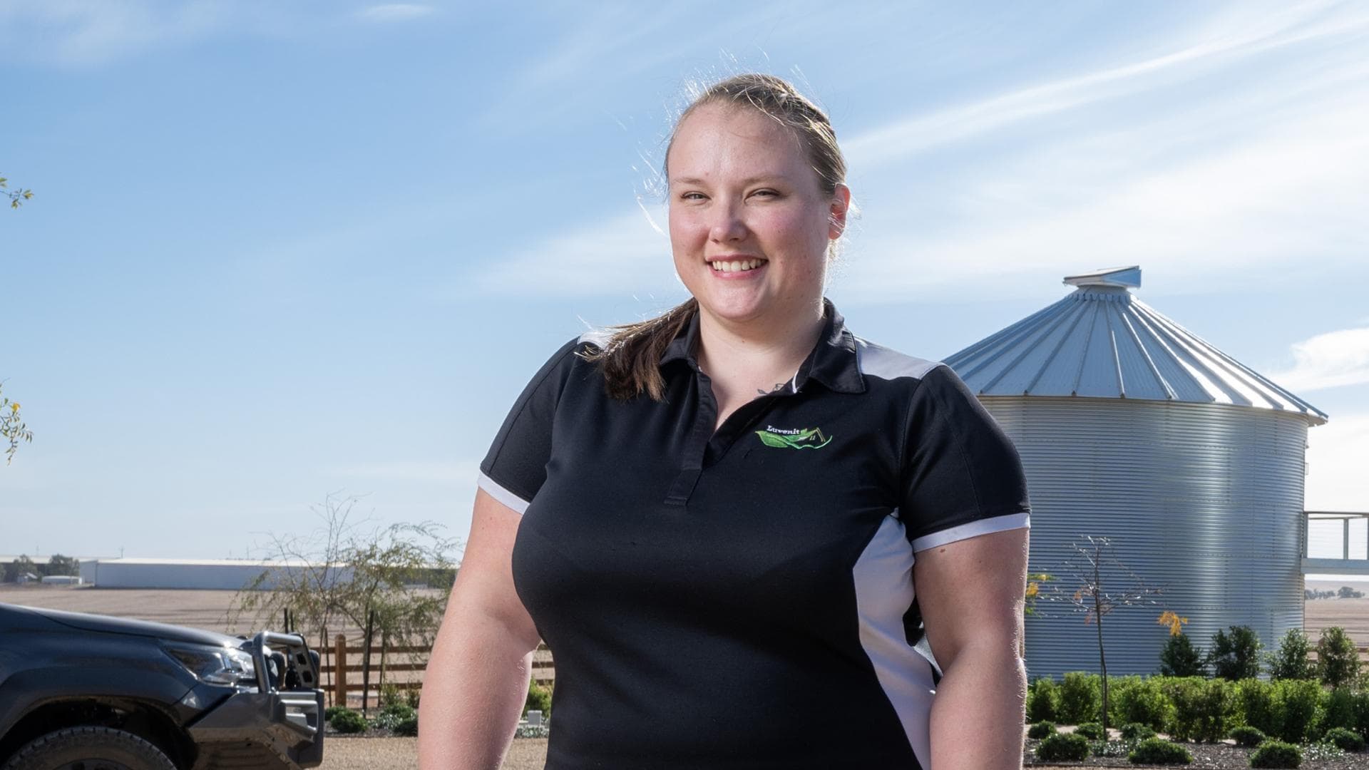 DES participant Ngaire smiles outside against a rural property and blue sky in her new work uniform