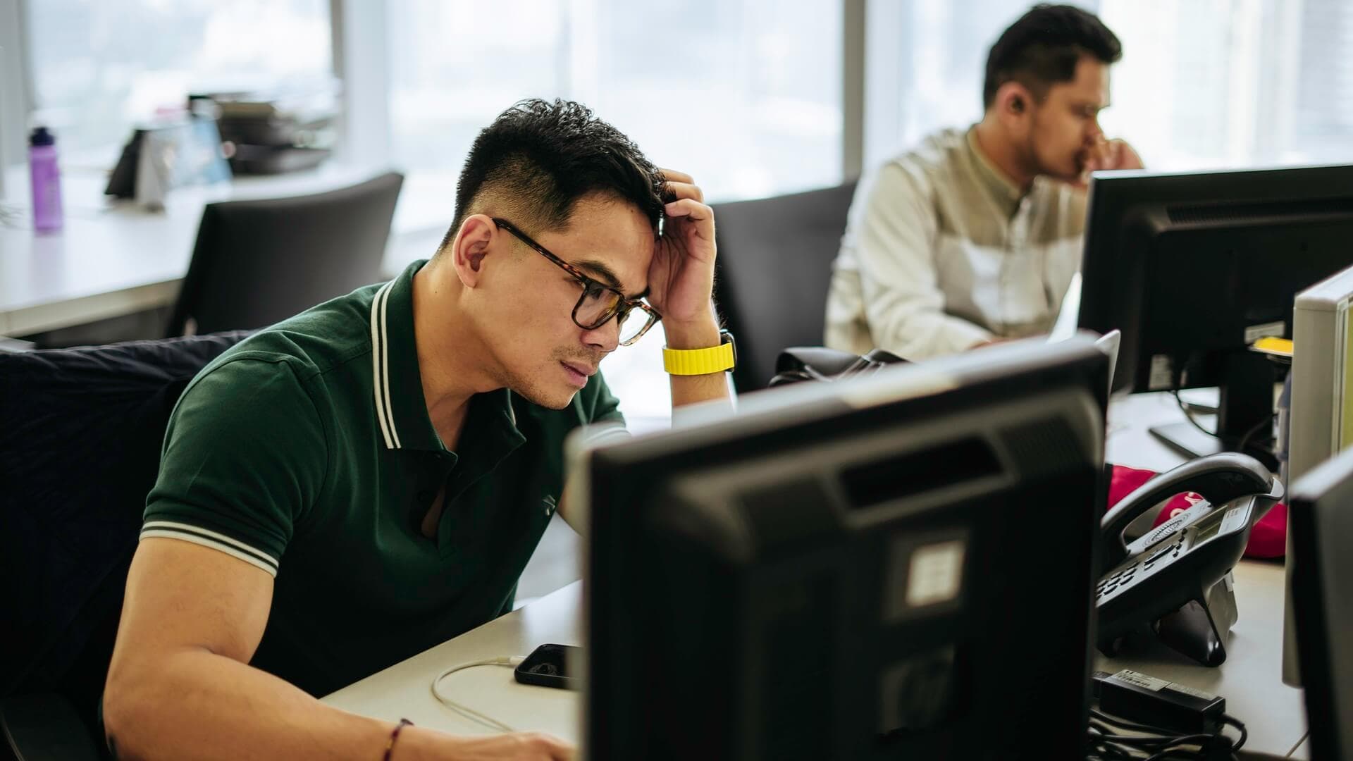 A stressed man trying to work on his computer at work