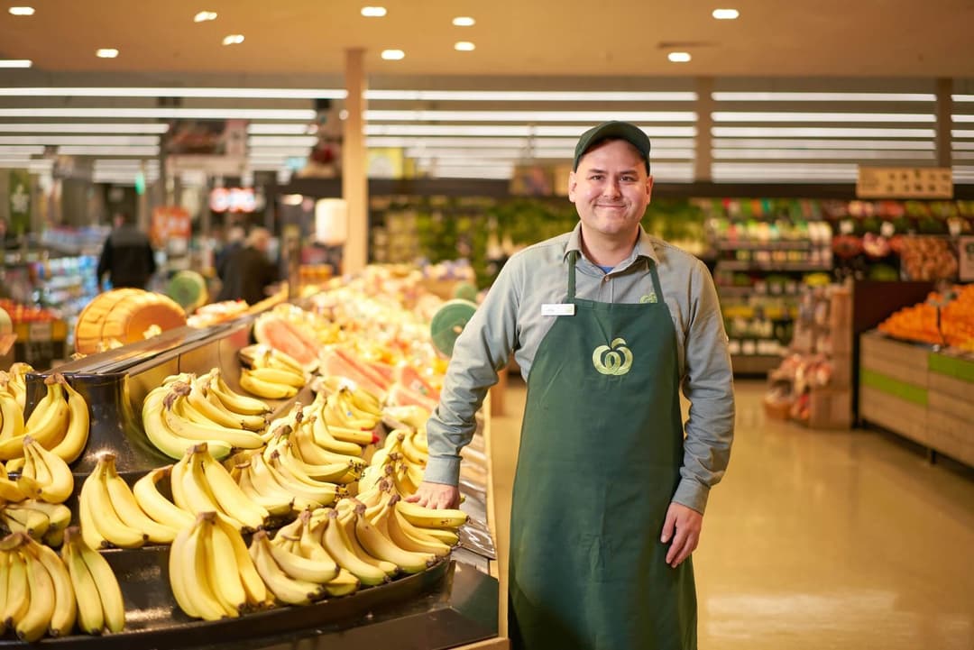 Young man who has found work at Woolworths standing next to a banana stand