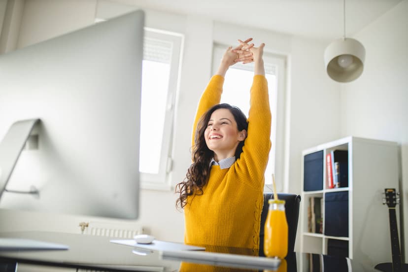 Woman in a yellow top stretches and smiles as she works from a desk