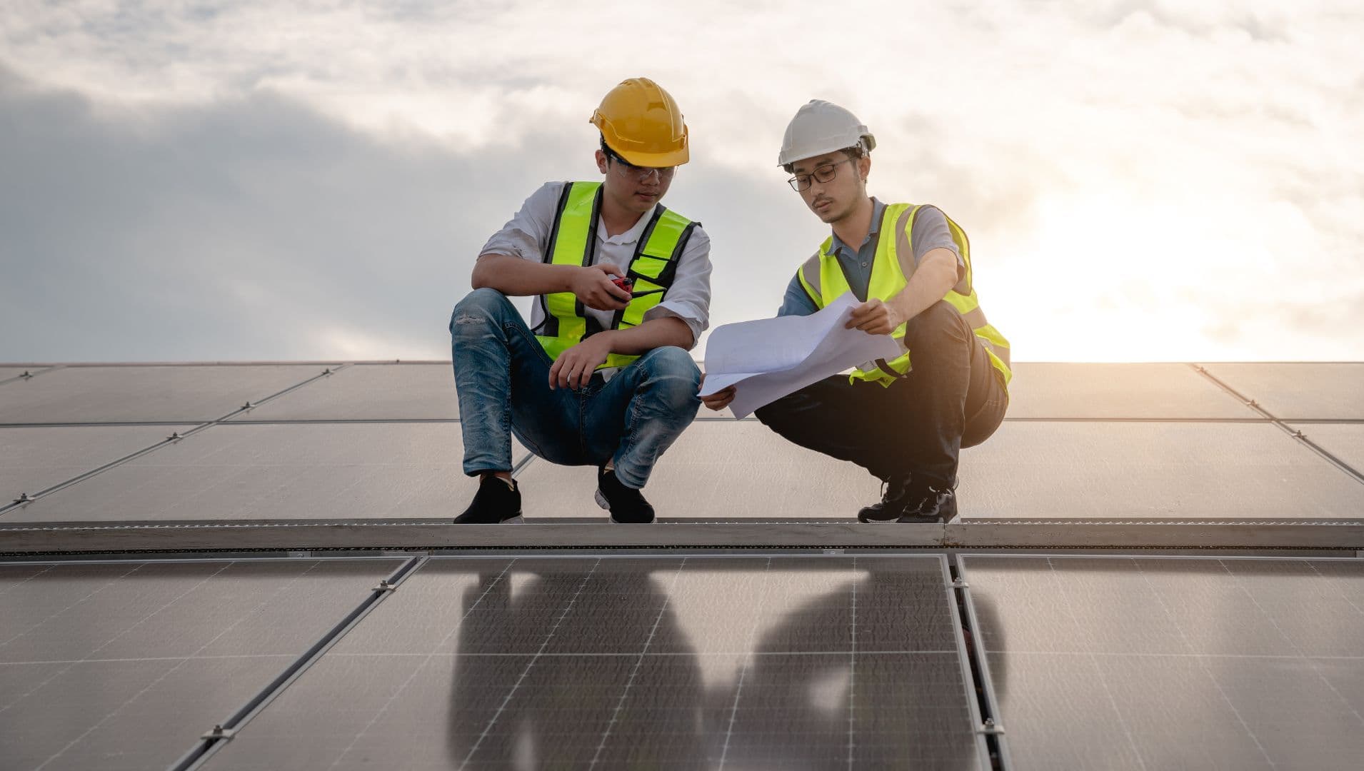 two workers look at plans on a solar panel rooftop