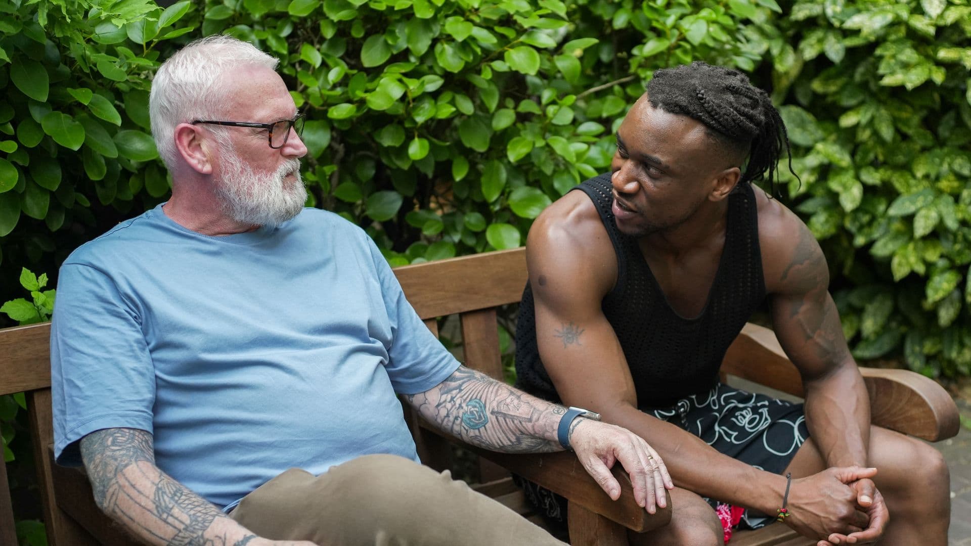 Khalif sitting on a wooden bench in a garden setting, talking with an advisor about his journey from repeated homelessness to achieving personal training qualifications through Ingeus support.