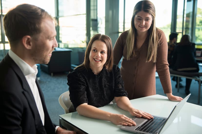 Three individuals engaged in a discussion around a laptop. Female hero looks to APM WorkCare Consultant smiling