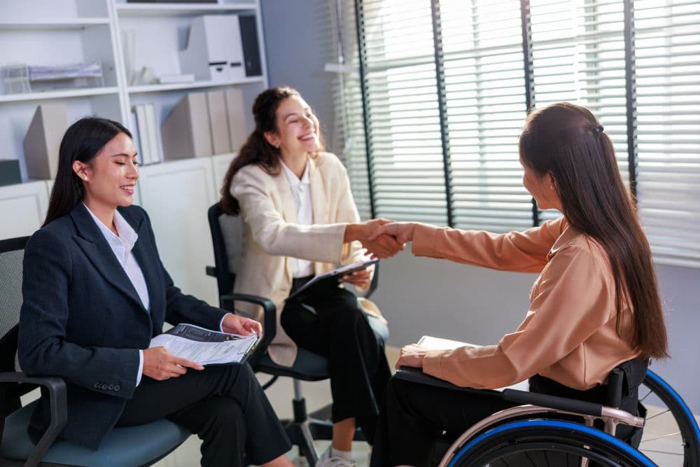Inclusive Job Interview with Candidate in Wheelchair Shaking Hands - stock photo A confident job candidate in a wheelchair shakes hands with a manager during an inclusive and successful job interview in a bright, modern corporate office.