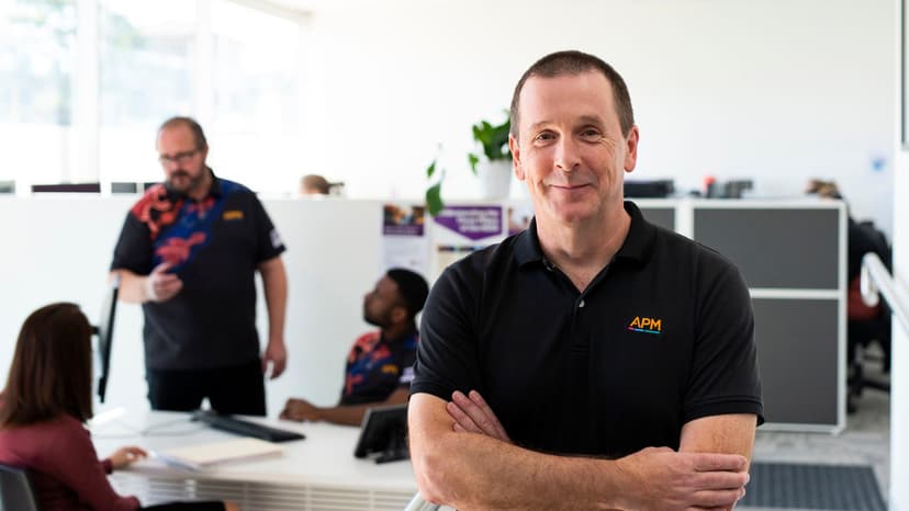 Simon from APM Communities stands in an office wearing a black APM polo.