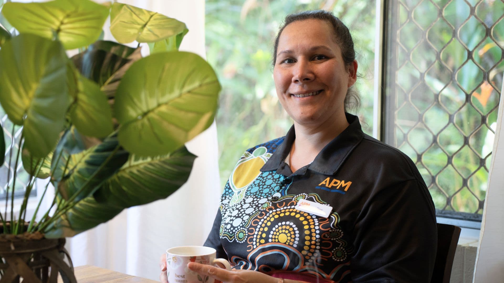 APM team member Dee in a First Nations top smiling with a coffee cup