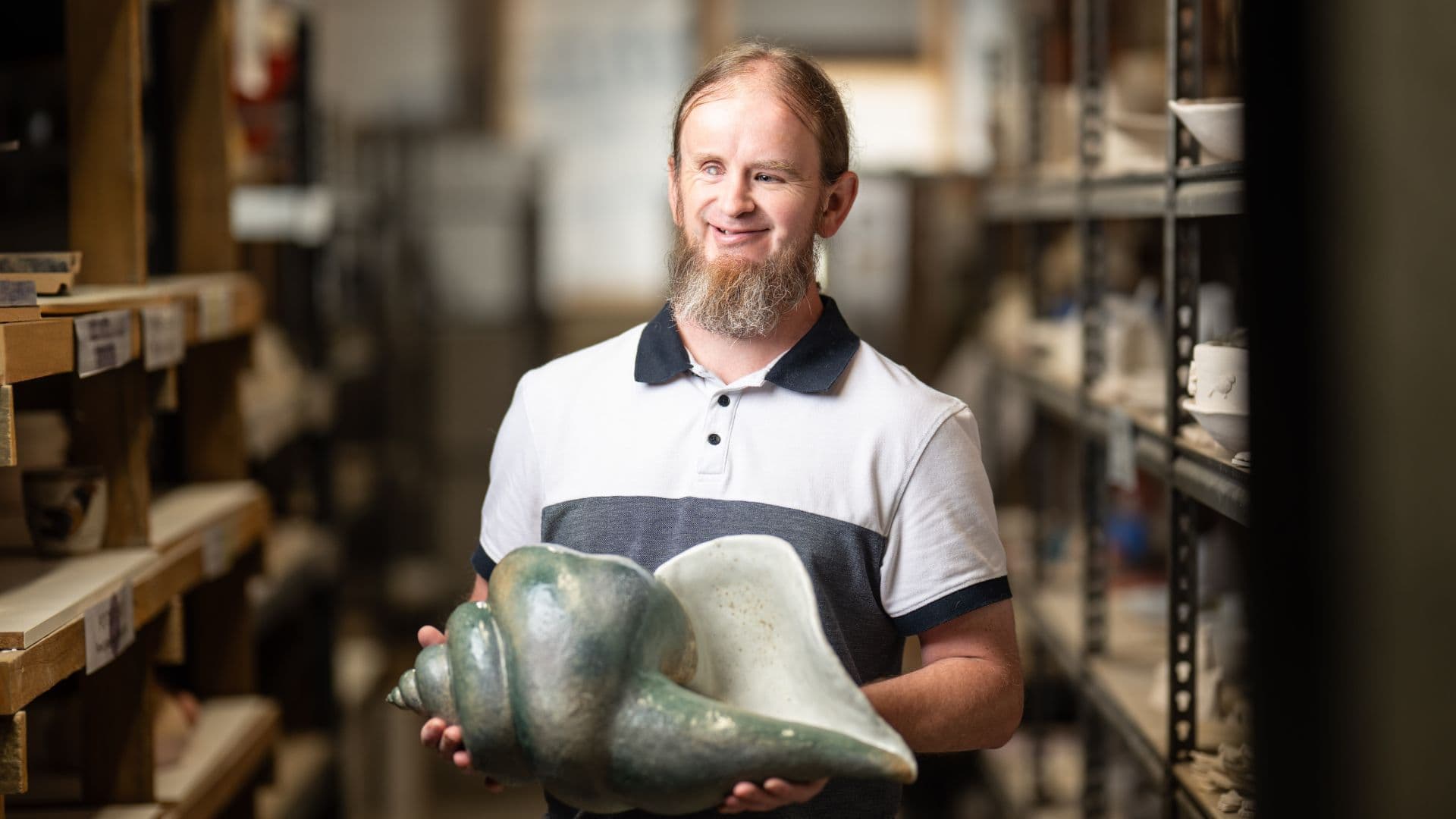 Ben standing and holding one artwork of a giant shell