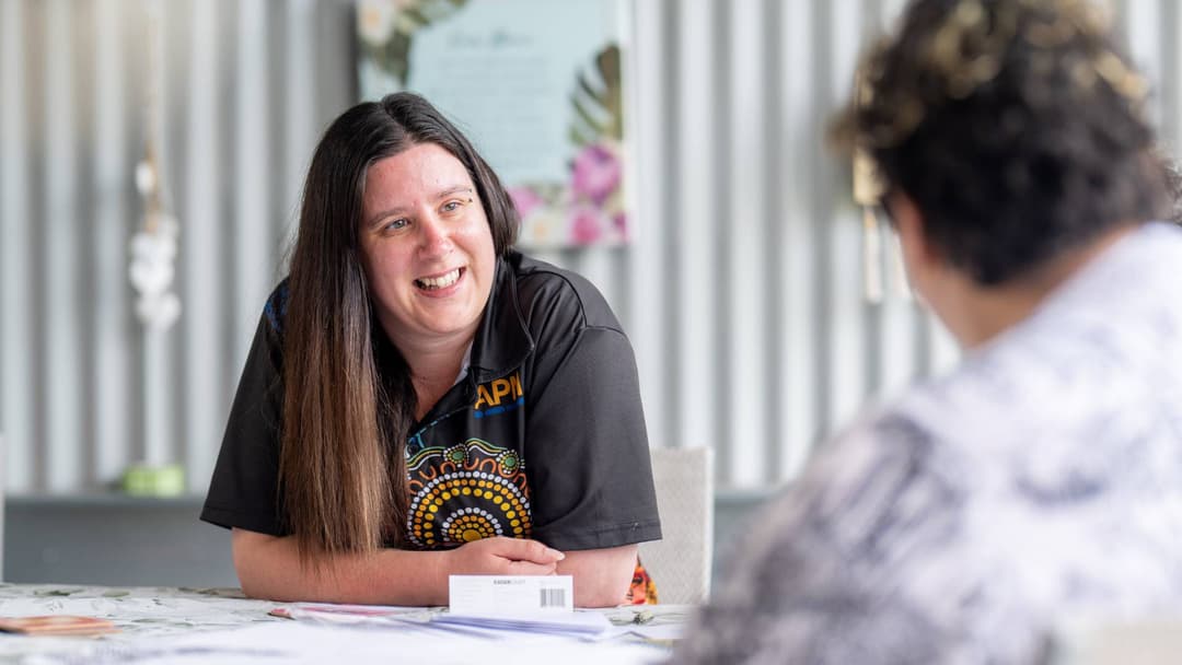 A woman in an APM top smiles at a table with a participant