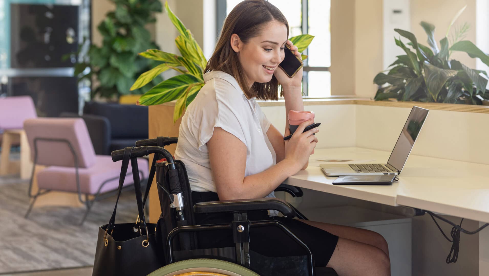 A woman in a wheelchair talking on her phone in front of a laptop