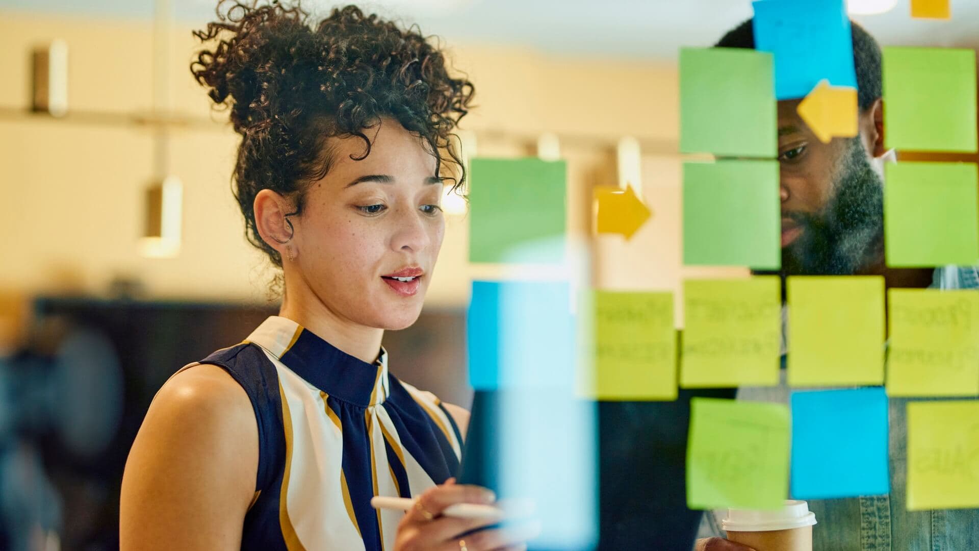 A woman sticking up different coloured post-it notes on a window at work