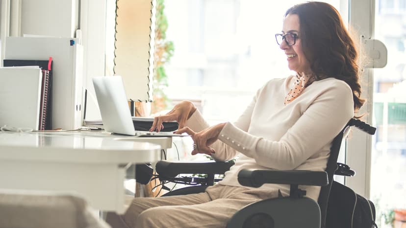 A woman with a physical disability sits at a desk in front of a computer