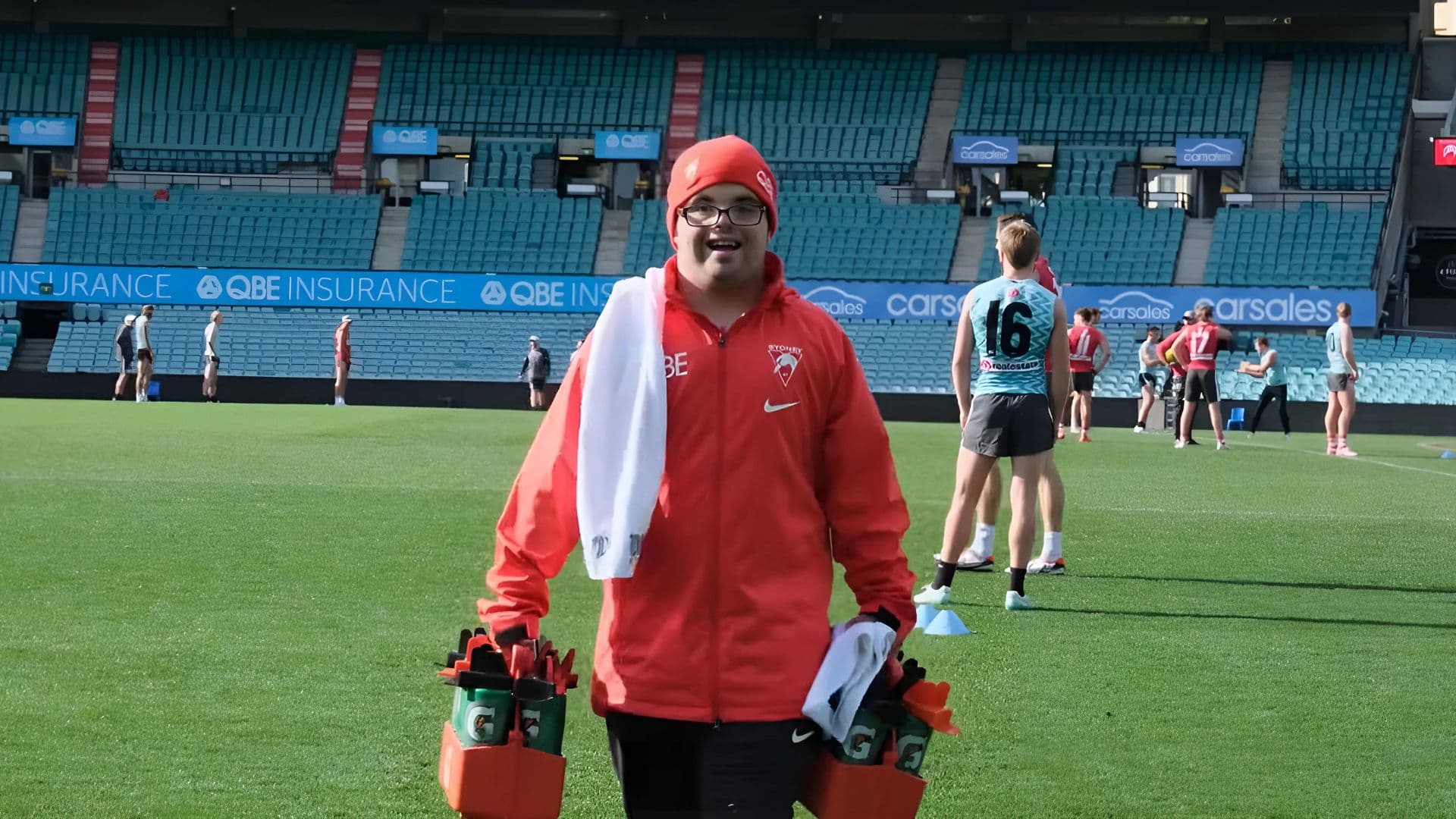 Adam wears his Sydney Swans employee kit as he delivers water bottles during traiining