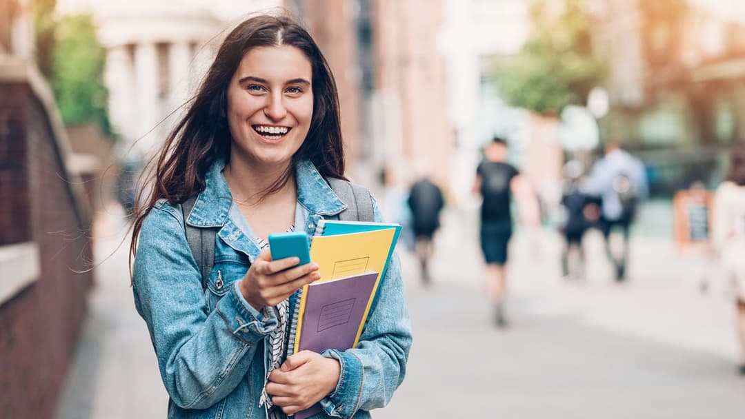 A student holding notebooks and a phone while walking along a campus pathway, showcasing APM Futures Tailored Support program.