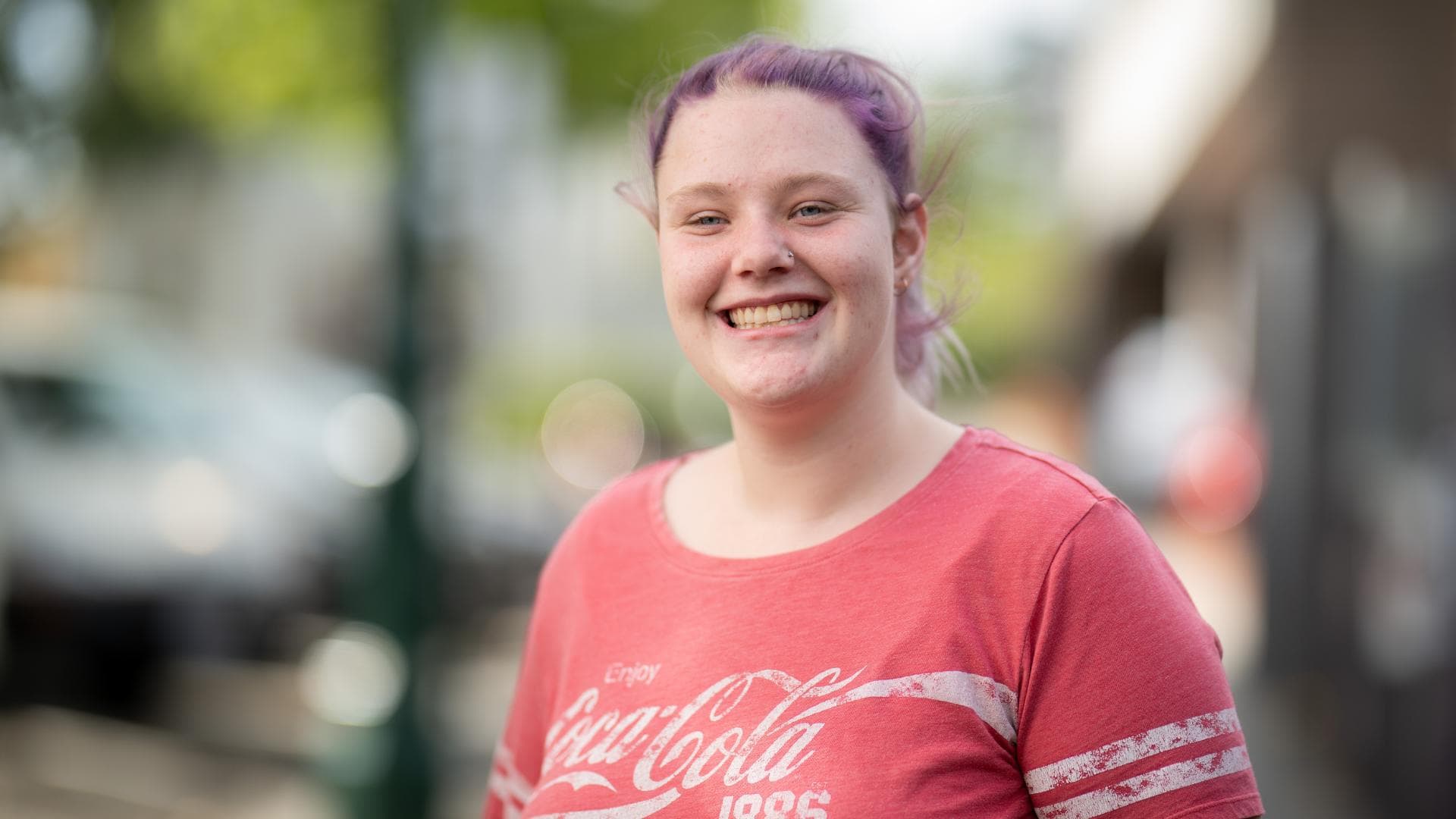 A young woman smiles in a red top outside an APM Workforce Australia branch