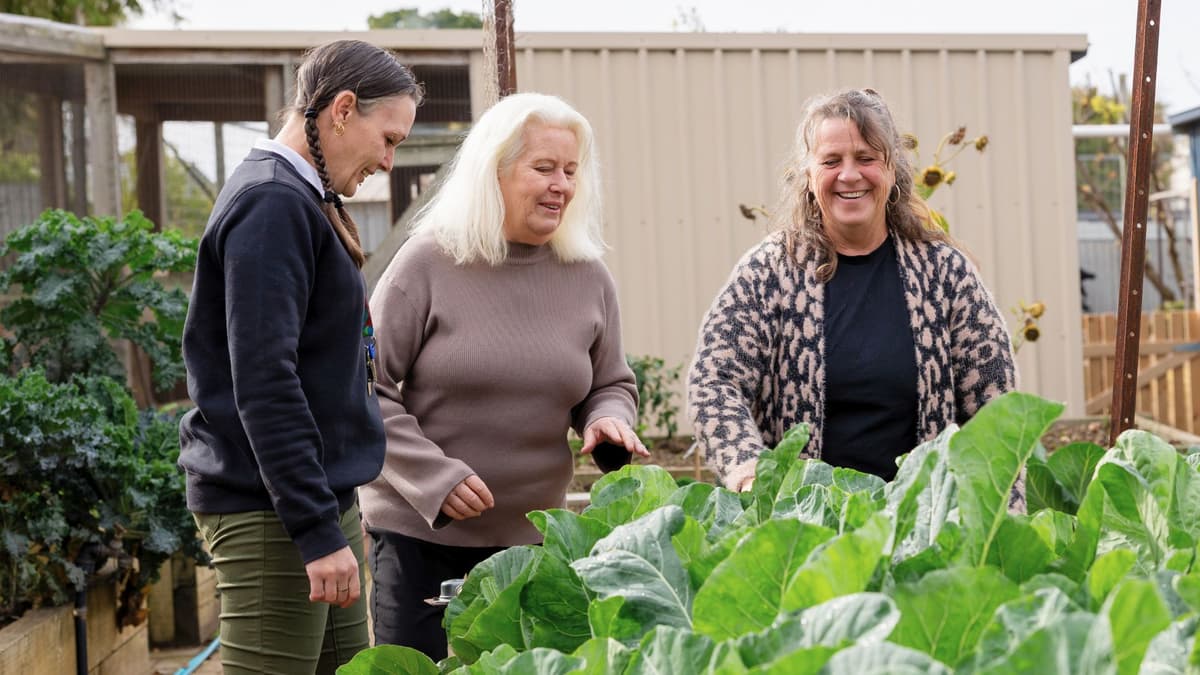 Kylie participates in an indoor activity, holding an insulated bag while another person reaches into a basket, highlighting community support through APM Workforce Australia.