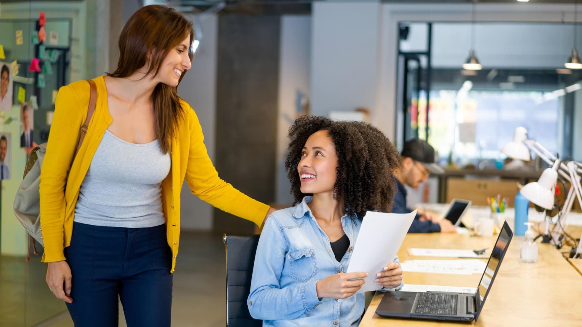 A woman talks to a co-worker as she walks past her desk