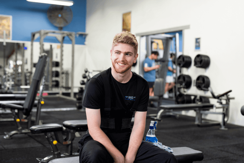 Nicholas smiling as he sits on a bench in a weights gym