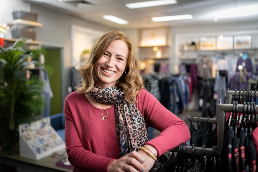 Emma smiles while leaning on a rack of clothes in the fashion store