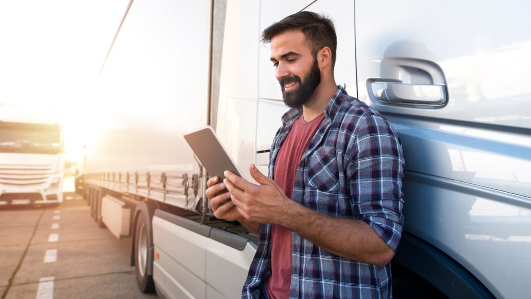 Man holds tablet while leaning on truck